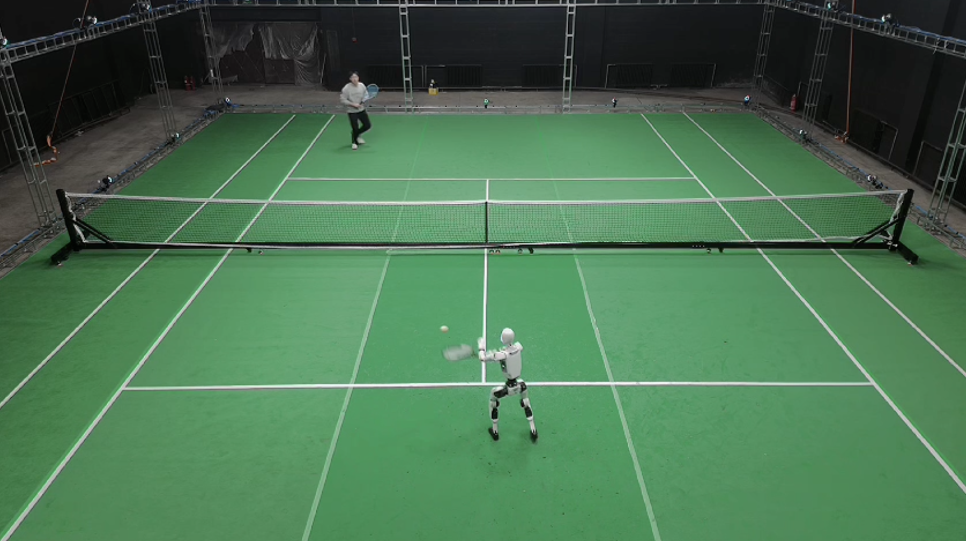 Humanoid robot playing tennis against a human player on an indoor court — LATENT Project